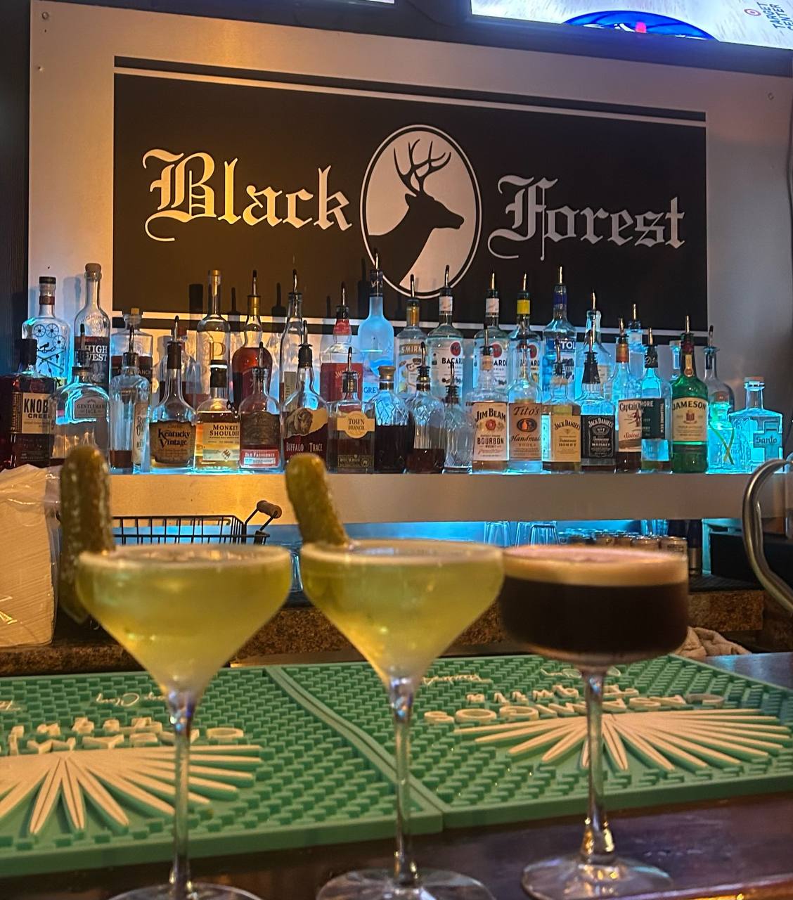Three cocktails lined up at the bar under the Black Forest sign