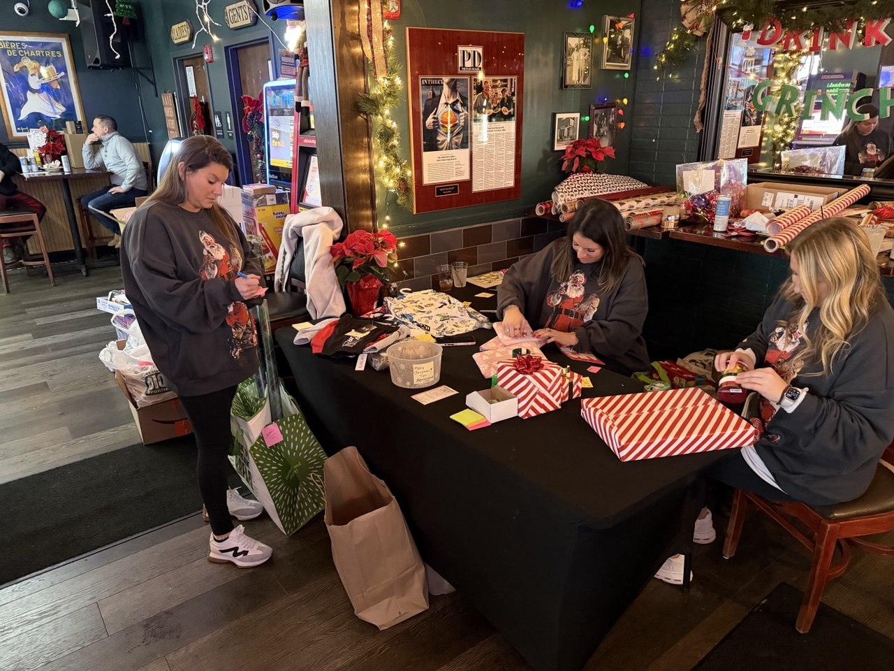 Volunteers in matching sweatshirts wrapping holiday gifts at the bar