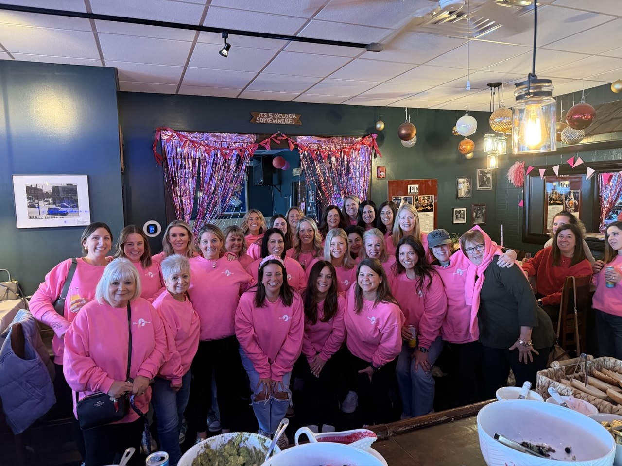 Large group in matching pink hoodies at the bar for a bachelorette party